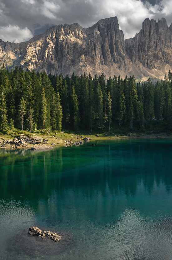 Lago alpino dalle acque color smeraldo circondato da foreste di conifere e pareti dolomitiche
