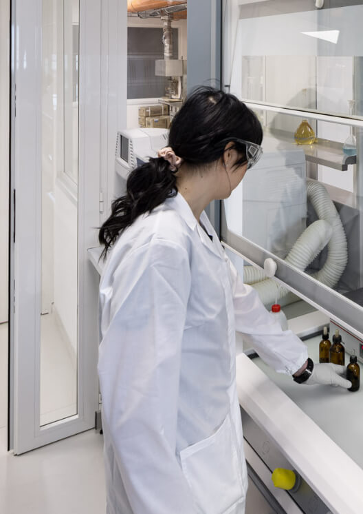 Ricercatrice in camice bianco che lavora sotto una cappa aspirante in laboratorio
