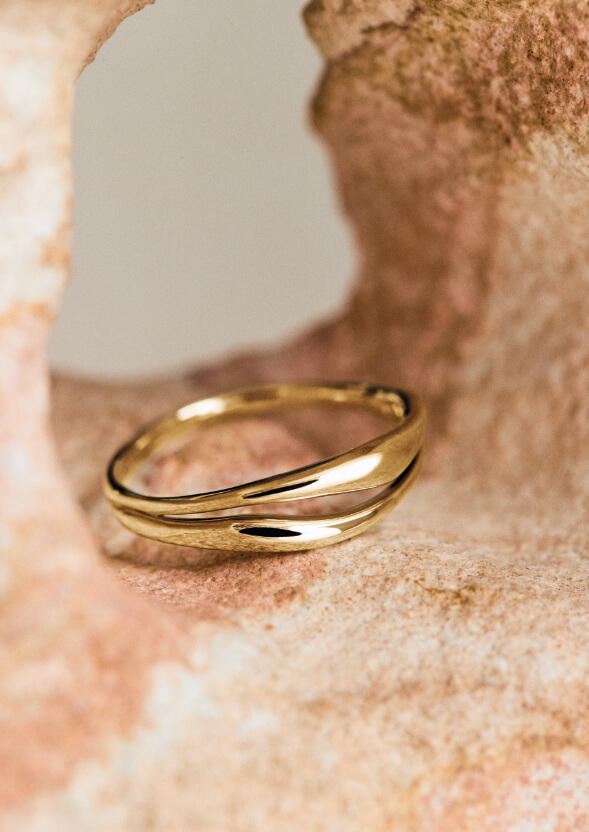 Anello in oro con design intrecciato appoggiato su una superficie in pietra